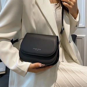 Sacoche selle en cuir noir avec texte blanc porté par un mannequin en blazer blanc