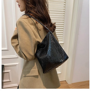 Detail of black crocodile embossed bucket bag on shoulder with sleek leather texture