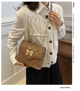Detail of brown quilted crossbody bag with golden bow clasp and metal chain strap