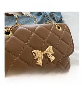 Detail of brown quilted leather handbag featuring a golden bow metal clasp and chain