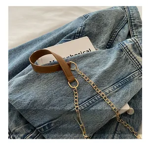Detail of crossbody bag strap featuring brown faux leather and golden metal chain link