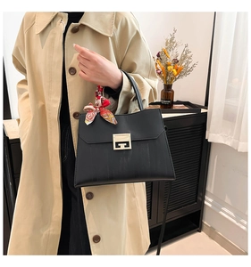 Detail of a matte black handbag with a gold buckle and decorative silk scarf handle