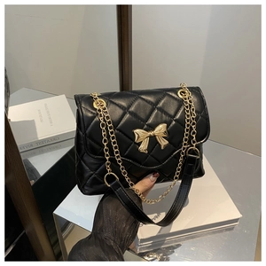 Close-up of quilted black leather texture with golden bow buckle on crossbody bag