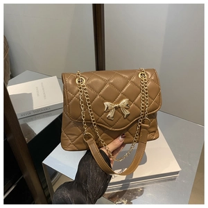 Detail showing brown quilted crossbody bag with a gold bow and metal chain strap