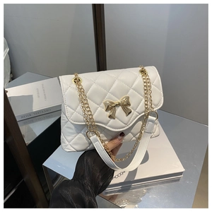 Detailed view of white quilted crossbody bag with gold bow clasp and chain strap