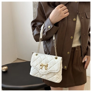 Detail of white quilted crossbody bag featuring a gold bow clasp and chain strap