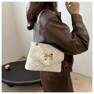 Detail of white quilted crossbody bag with gold bow buckle and chain strap on shoulder