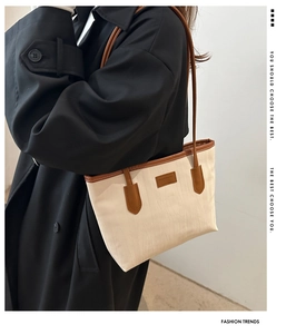 Minimalist cream tote bag with brown straps styled on a black trench coat for daily commute