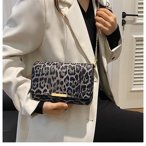 Detail of grey leopard print crossbody bag with gold chain strap on a white blazer