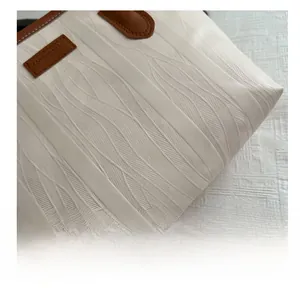 Detail of ivory tote bag with vertical wavy texture and brown leather logo tag