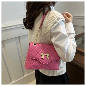 Pink quilted crossbody bag with gold bow detail worn by a model in a modern room