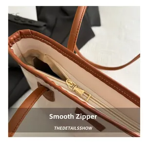 Detail view of smooth golden zipper and premium brown leather trim on beige tote bag