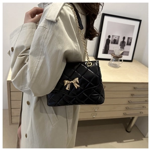 Detail of black quilted crossbody bag featuring a golden bow buckle and chain strap
