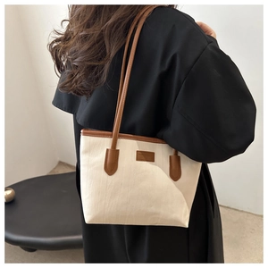 Detail of canvas tote bag with brown leather trim worn over a woman's shoulder