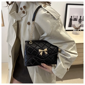 Close-up of quilted black shoulder bag with gold bow clasp and chain strap detail
