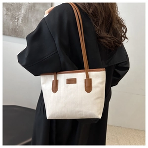 Detail view of large white canvas tote bag with brown straps worn over a black coat