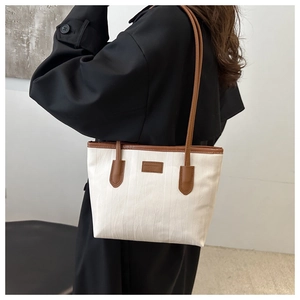 Detail of white striped tote bag with brown leather handles and brand logo patch