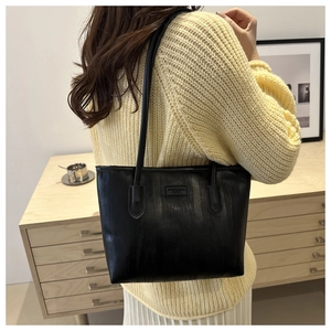 Detail of black tote bag with vertical stripes texture worn on shoulder over yellow sweater