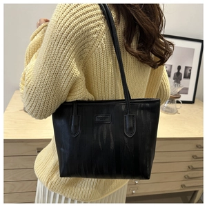 Detail of black tote bag with unique flame texture and brand label on model shoulder