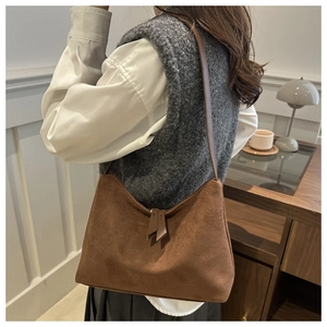 Close-up of caramel suede shoulder bag with tassel detail worn over a white shirt