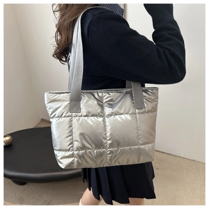 Macro detail of silver quilted metallic puffer tote bag with wide grey shoulder straps