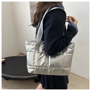 Détail d'un grand sac fourre-tout matelassé argenté porté à l'épaule par un mannequin