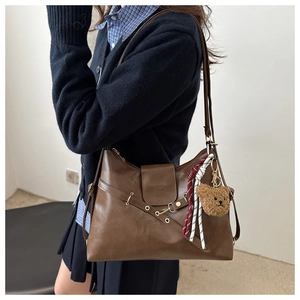 Detail of brown leather tote bag featuring eyelets, bear charm and shoulder strap