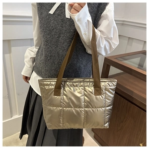 Quilted metallic champagne gold tote bag with wide brown woven strap on a model shoulder