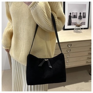 Detail of a black suede underarm bag with metal zipper worn by a model in a home setting