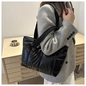 Side view of a black quilted down tote bag worn as a shoulder bag in minimalist room