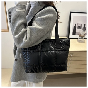 Detail of black quilted down tote bag in shiny fabric styled with a wool blazer