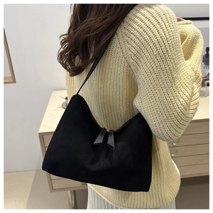 Detail view of a black suede underarm bag featuring dual long zippers on a textured surface