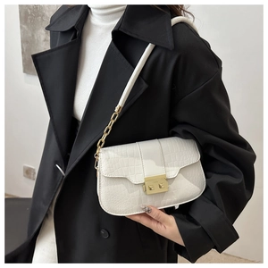 White crocodile pattern crossbody bag with gold snap closure and chain strap on a model