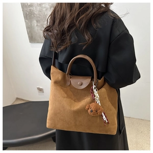 Détail d'un sac cabas en daim marron avec poignée en cuir et un joli porte-clés ours