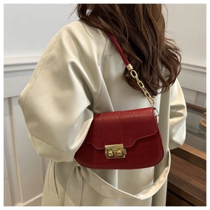 Detail of red crocodile pattern shoulder bag with gold clasp worn with a beige coat