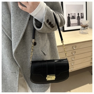 Detail of black crocodile pattern saddle bag with gold clasp and chain strap on grey coat