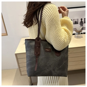 Detail of dark grey canvas tote bag with brown leather handles and brand tag