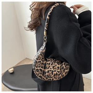 Detail of leopard print crescent bag with gold clasp worn over a black wool coat