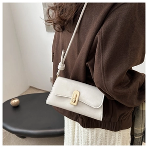 Detail of white rectangular shoulder bag with golden U-shaped lock and knotted strap detail