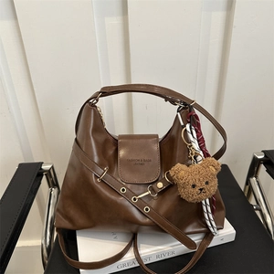 Vintage brown leather hobo tote bag with teddy charm on a stylish chair