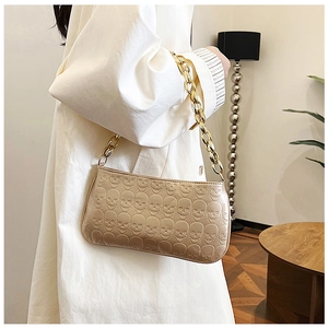 Detailed view of beige baguette bag featuring embossed skull pattern and gold chain strap