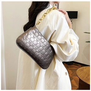 Close-up of metallic gray skull embossed crossbody bag with thick gold chain strap
