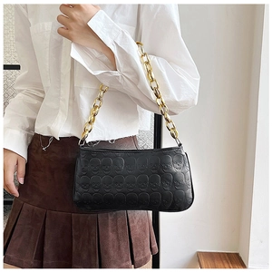 Detail of the black leather bag featuring gothic skull embossing and thick gold chain strap