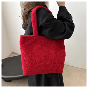 Detail of high-capacity red faux shearling tote bag worn over a black winter wool coat