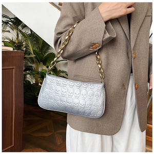 Close-up of silver shoulder bag with embossed skull texture and chunky gold chain strap