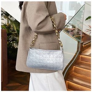 Detailed side view of silver skull embossed handbag with thick gold chain on a model