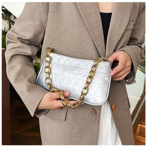 Close-up of silver skull embossed handbag with chunky gold metal chain strap detail