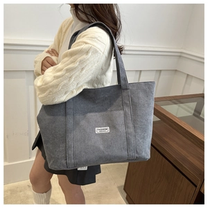 Detail of grey corduroy tote bag with front pocket and white fashion label on shoulder