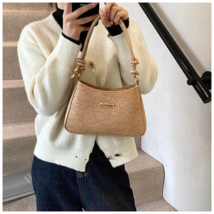 Detail of lace embossed texture on beige baguette bag with knotted handle and gold buckle