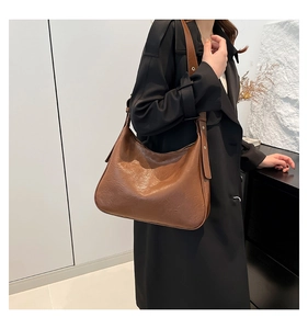 Detail of a brown pleated leather tote bag with a wide eyelet shoulder strap on a model